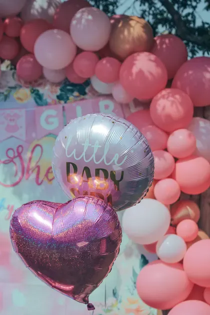 A lush blush and pink balloon arch with foil heart balloons and a baby sign.