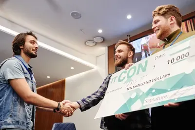 Two coworkers shake hands holding an oversized prize check at a company awards night.